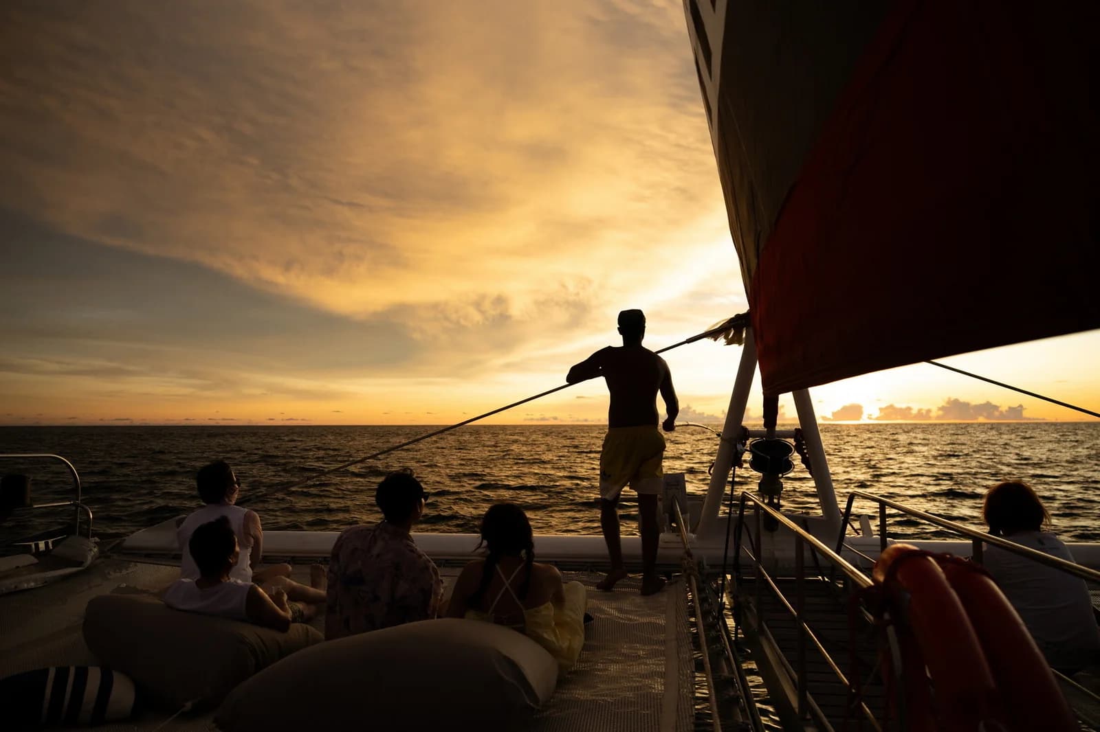 Silhouetted guests on the yacht bow beneath a golden sunset sky