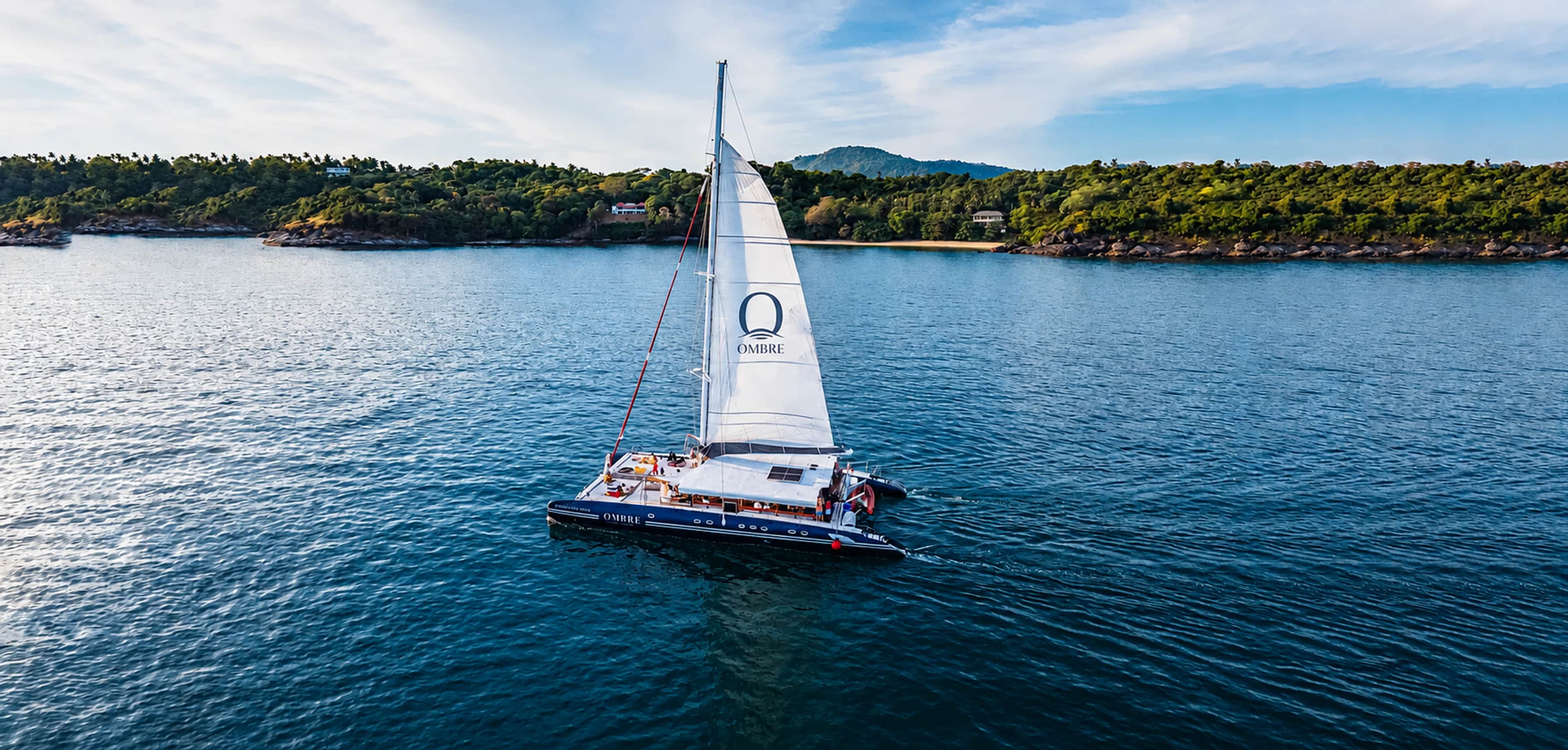 The navy OMBRE catamaran with its branded white sail on the Andaman Sea